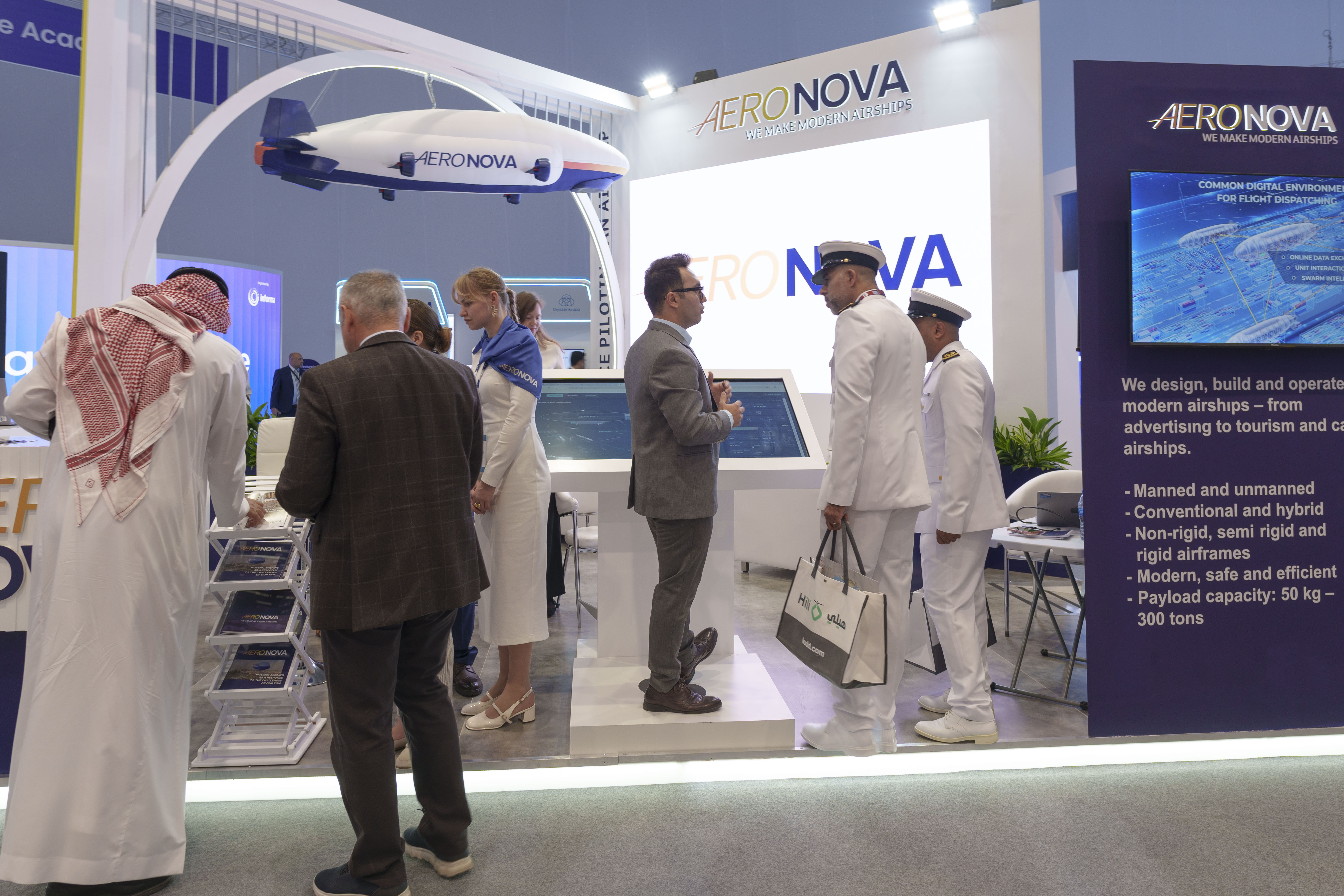 Booth wide view · airship scale model overhead, Saudi visitors on the floor
