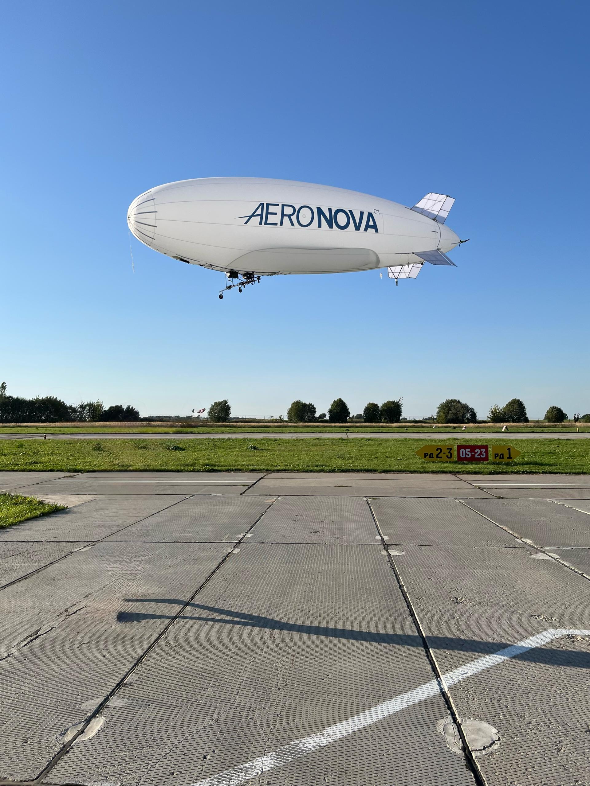 NOVA-01 in flight over the airfield · runway markings visible